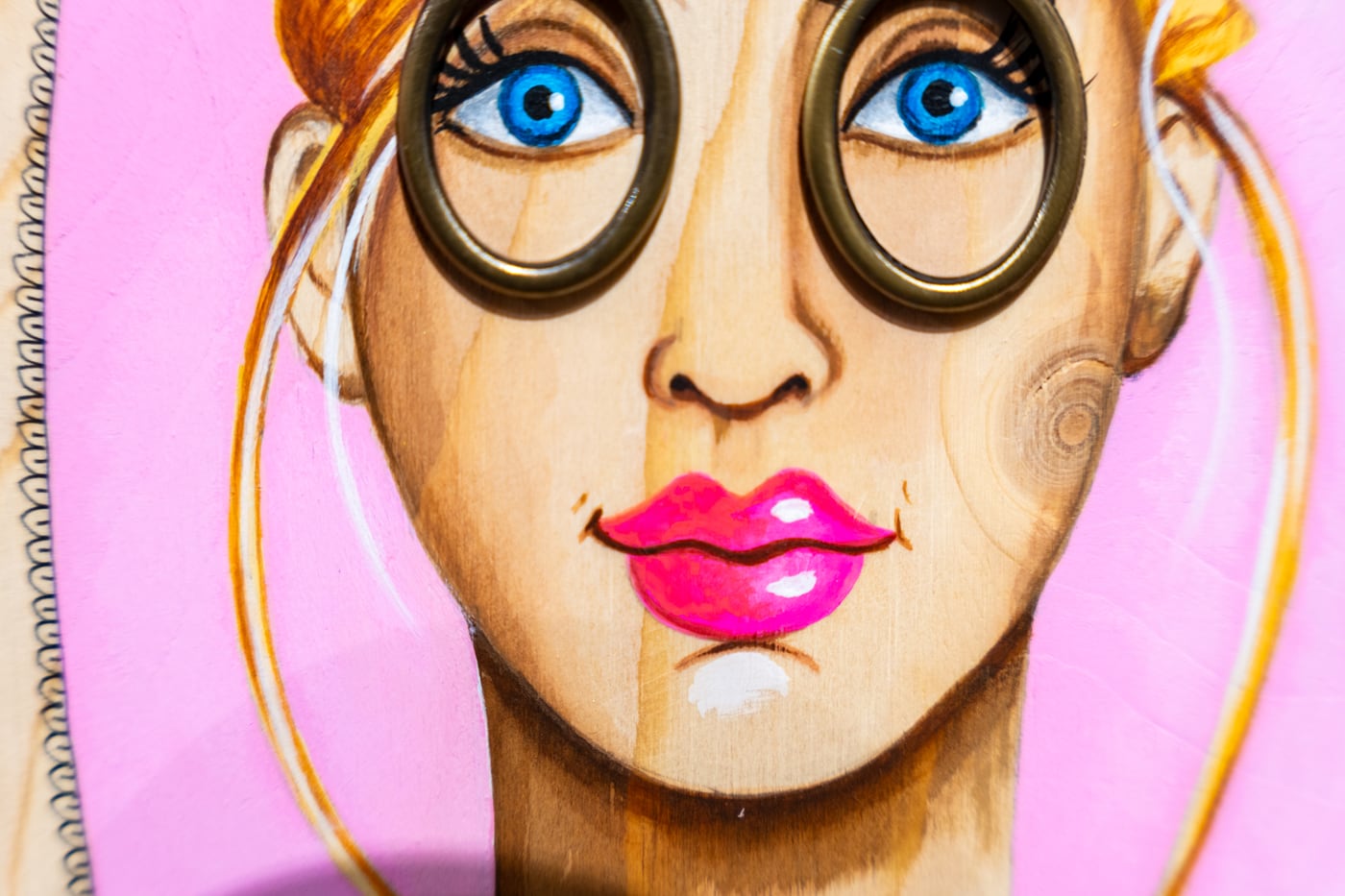Visage peint sur bois par Laure C., lorgnette dorée, yeux bleus et fond rose