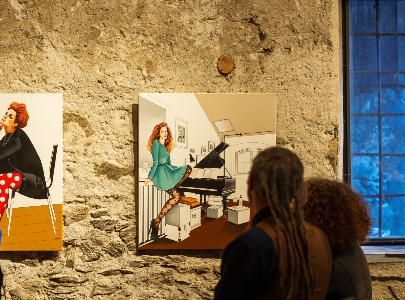 Toile de Laure C. accrochee sur un mur de pierre, deux visiteurs vus de dos